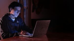 Seorang remaja sedang mengetik di laptop dengan cahaya biru lembut — simbol suara pertama yang muncul di dunia digital.