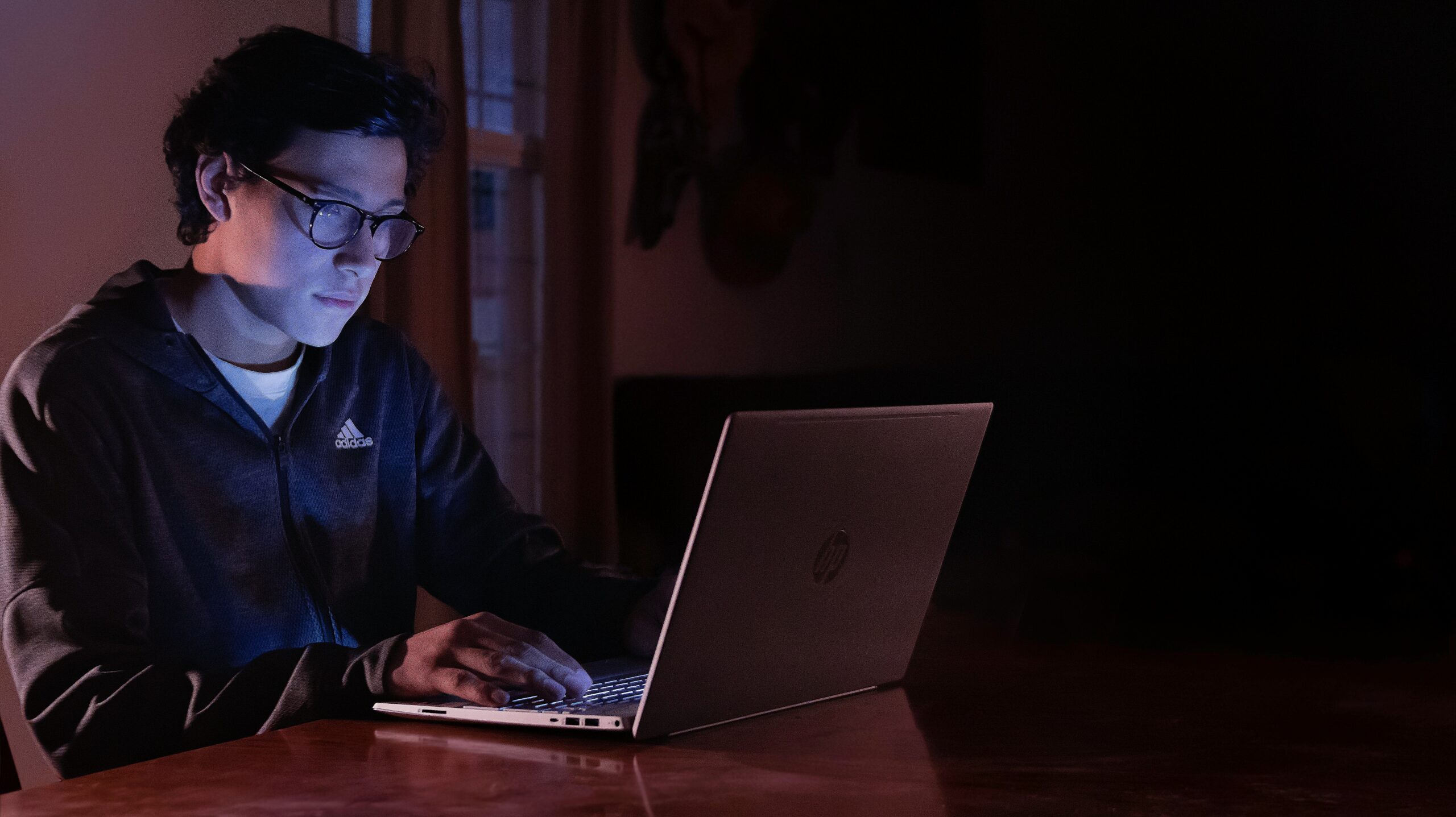 Seorang remaja sedang mengetik di laptop dengan cahaya biru lembut — simbol suara pertama yang muncul di dunia digital.